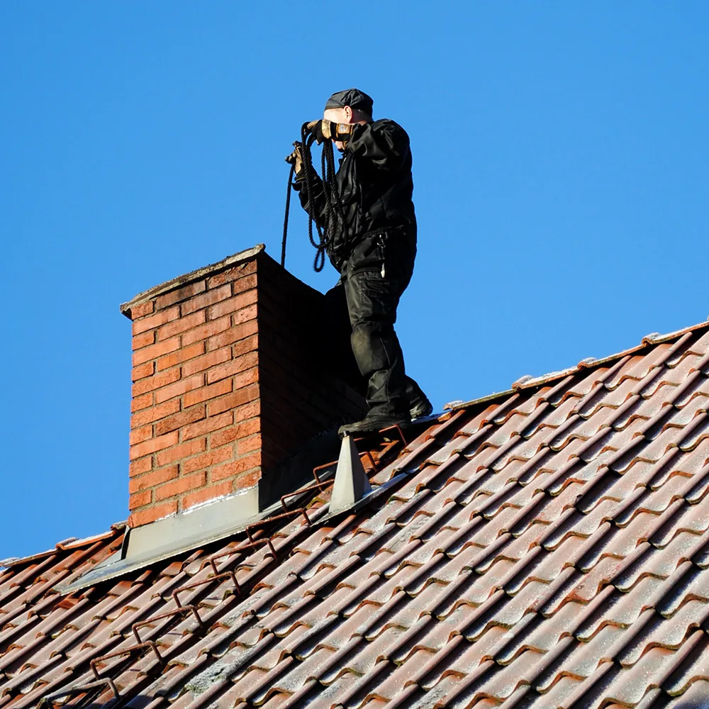 Illustrative chimney service equipment positioned beside a rooftop flue